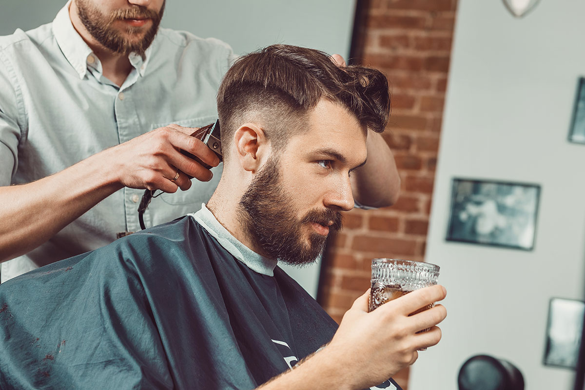 Young handsome barber making haircut of attractive bearded man in barbershop